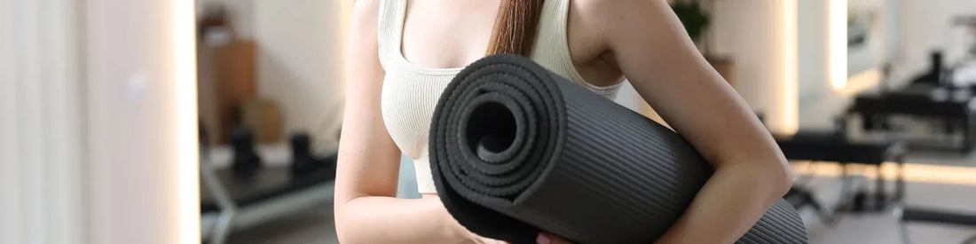 Femme tenant un tapis de pilates noir dans un studio moderne