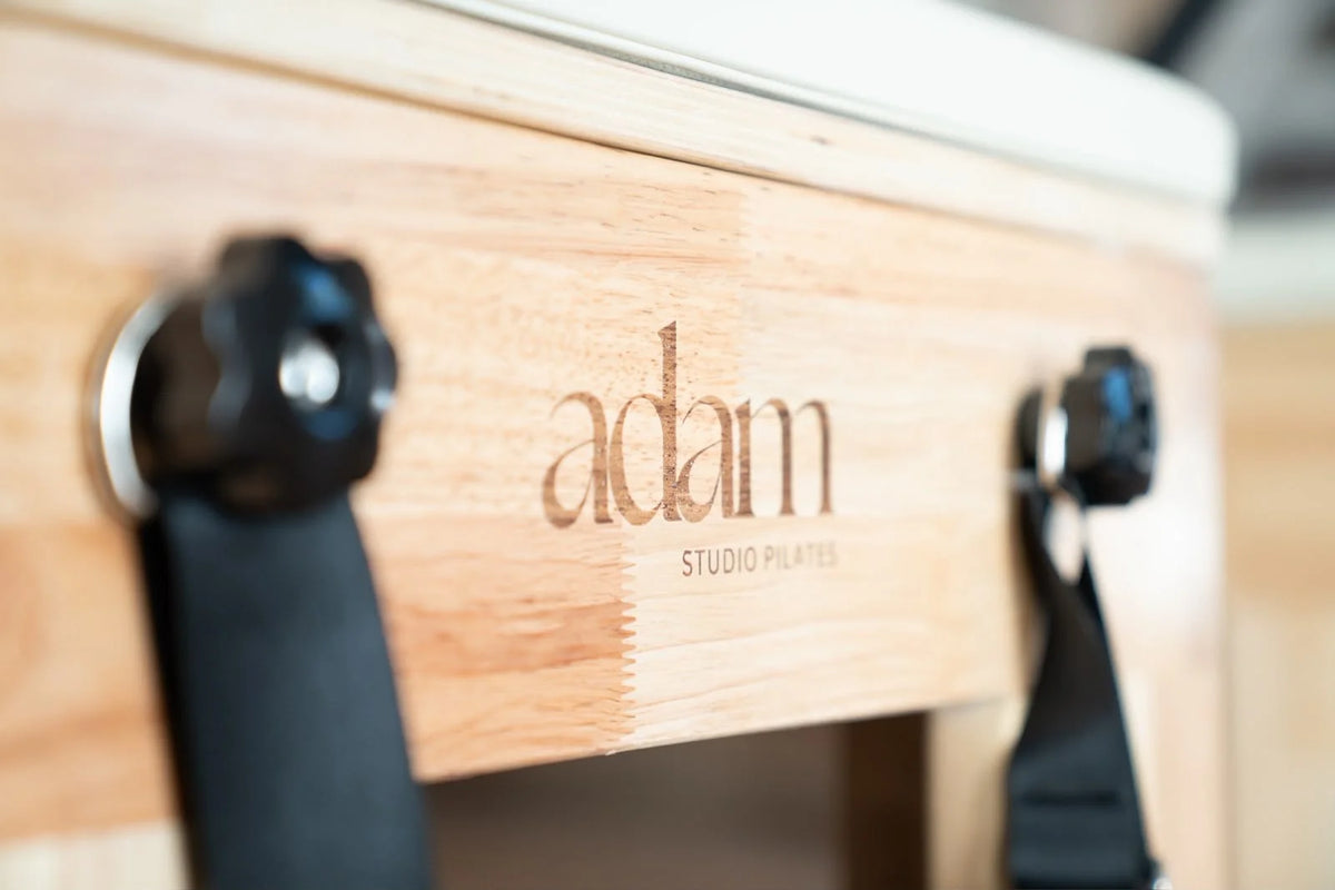 Logo Adam Studio Pilates gravé sur reformer en bois