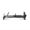 Reformer Pilates aluminium studio pro noir, vue de profil avec repose-pieds et carriage - Pilates At Home