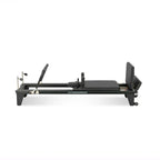 Reformer Pilates aluminium studio pro noir, vue de profil avec repose-pieds et carriage - Pilates At Home