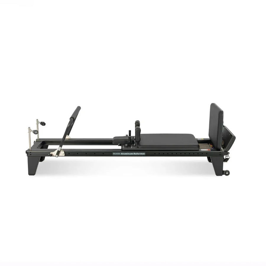 Reformer Pilates aluminium studio pro noir, vue de profil avec repose-pieds et carriage - Pilates At Home