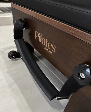 Détail du reformer Pilates At Home en chêne avec sangle et barre de poussée noire