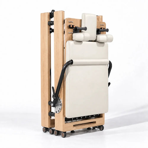 Reformer Pilates pliable en position repliée, cadre bois clair et rembourrage crème avec roulettes - Pilates At Home