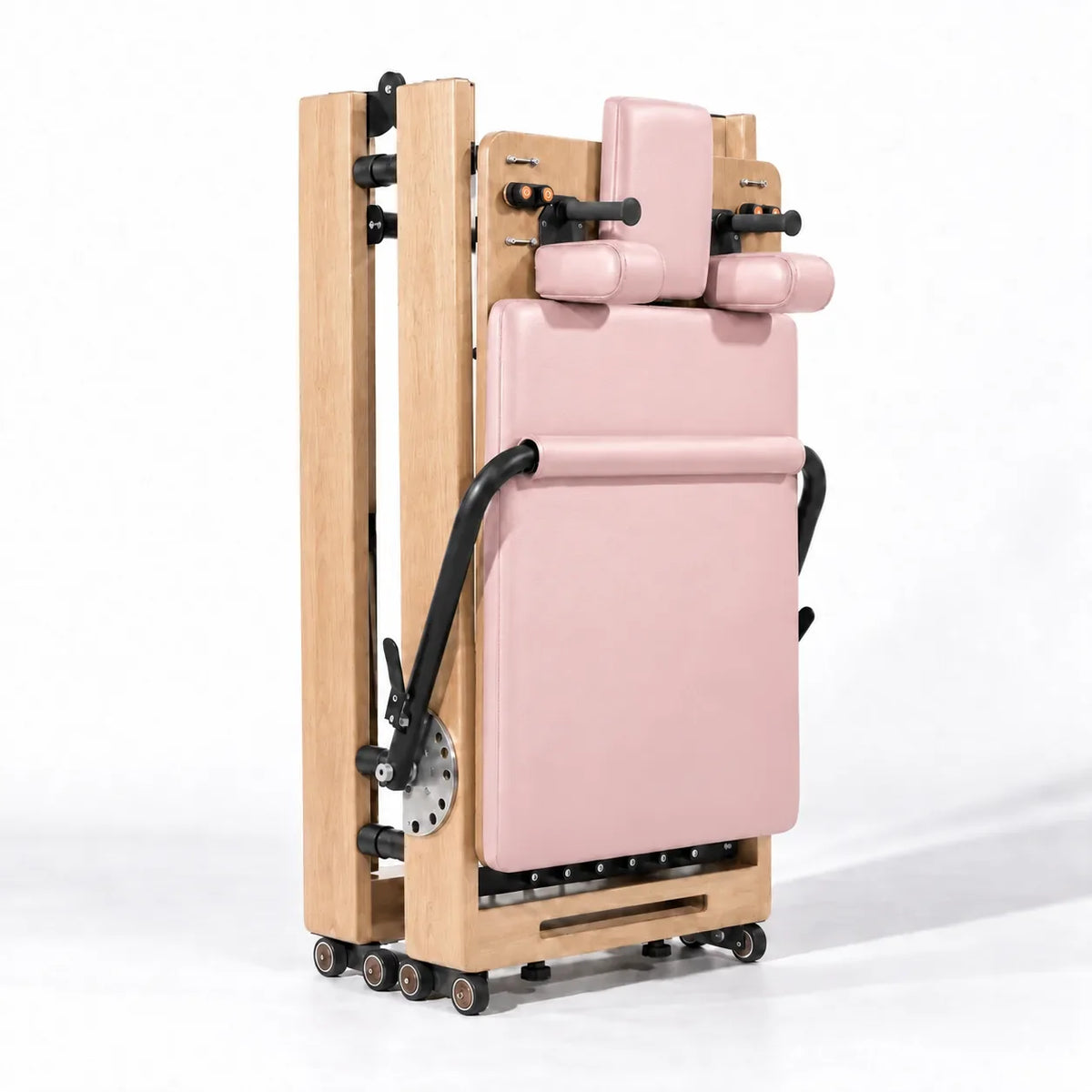 Machine Reformer Pilates pliable en bois clair avec revêtement rose, vue compacte repliée sur roulettes - Pilates At Home