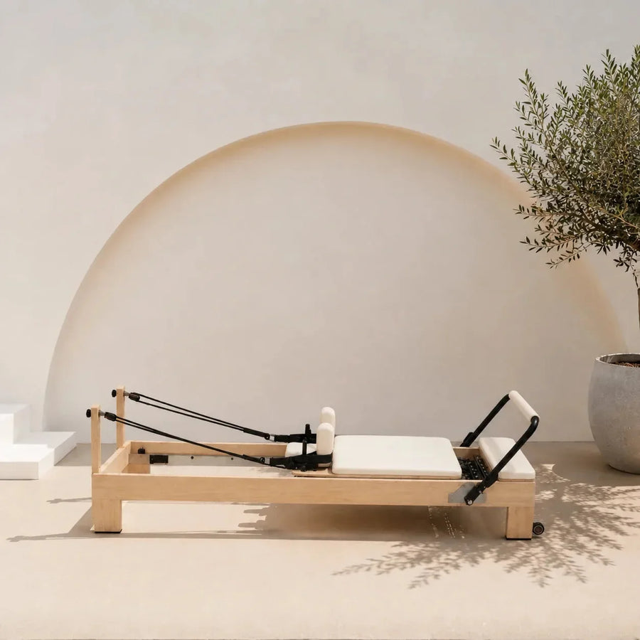 Reformer Pilates studio cadre bois naturel assise blanche avec cordes et repose-pieds, design épuré - Pilates At Home