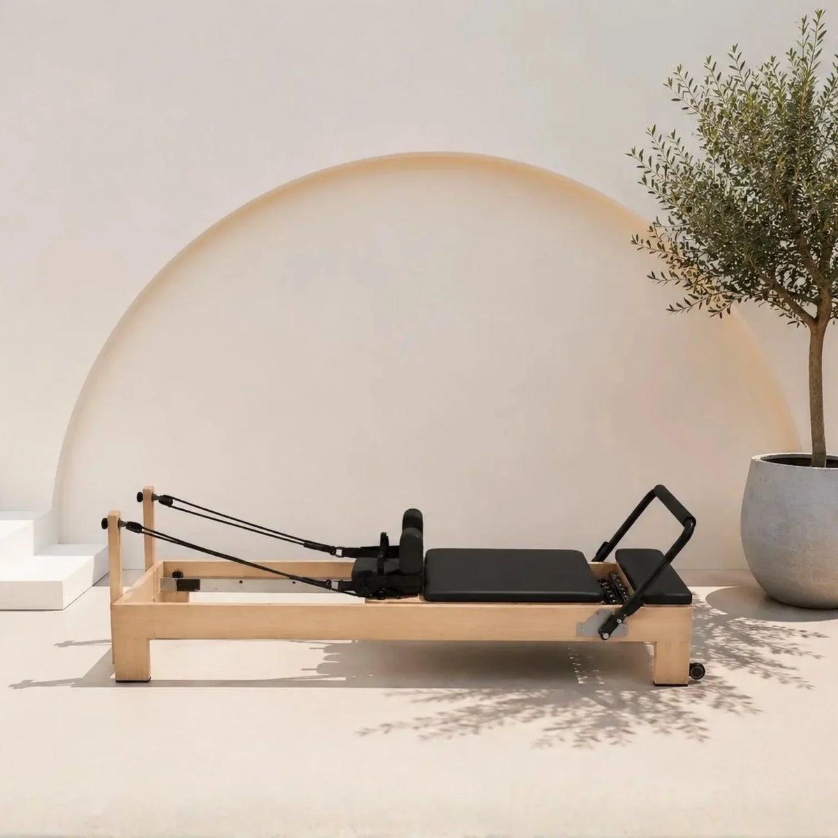 Reformer Pilates studio cadre bois clair carrossage noir avec sangles et repose-pieds, vue de profil - Pilates At Home
