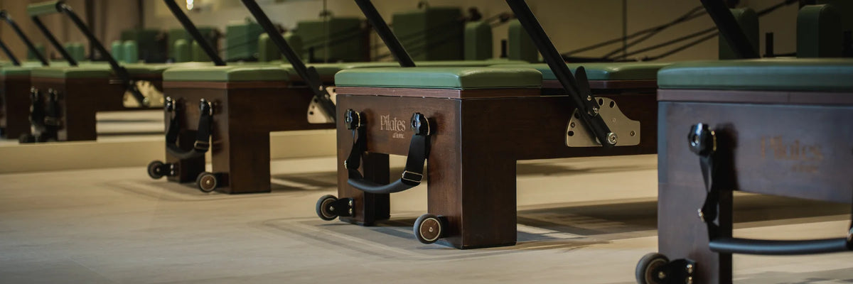 Rangée de machines Reformer Pilates At Home en bois avec coussin vert dans un studio professionnel