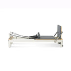 Reformer Pilates Studio Signature en aluminium blanc avec carrosserie grise et footbar réglable, vue de profil - Pilates At Home